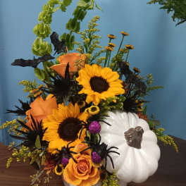 Orange and yellow floral arrangement in a white pumpkin container with black spider decorations