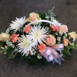 Basket arrangement of white spider mums, peach roses, and pink carnations with a ribbon handle