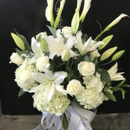 White lilies and roses arranged in a glass vase with a white ribbon