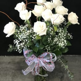 White roses arranged in a glass vase with baby's breath and a heart ribbon