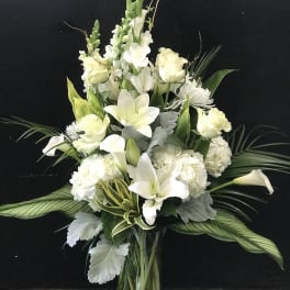 White floral arrangement in a clear glass vase with lilies and calla lilies