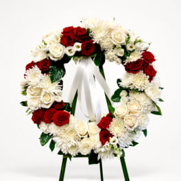 Circular wreath of red and white flowers on an easel with a white ribbon