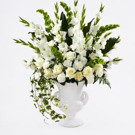 White floral arrangement in a white urn vase with trailing greenery