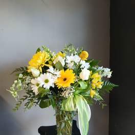 Yellow and white mixed bouquet in a clear glass vase with a green ribbon