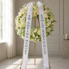 White floral funeral wreath with two memorial ribbons on a stand