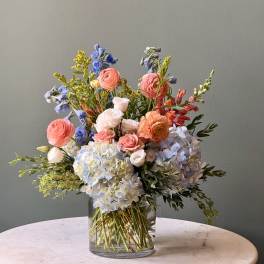Mixed bouquet in a clear glass vase with pastel pink, blue, and white blooms