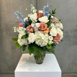 Wedding bouquet in a glass vase with white, peach, and blue flowers