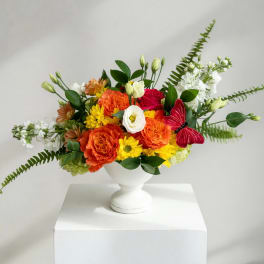 Colorful bouquet in a white pedestal vase with orange, yellow, red, and white blooms