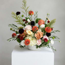Mixed bouquet in a white bowl vase with peach, white, orange, and burgundy flowers