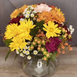 Mixed bouquet of yellow, orange, pink, and white flowers in a clear glass vase