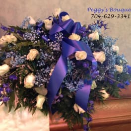 White roses and blue flowers arranged with a purple ribbon