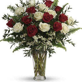 Red and white roses in a clear glass vase with fern foliage