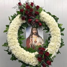 Circular funeral wreath of white flowers and red roses with a religious portrait in the center