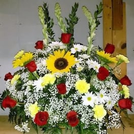 Large funeral spray with red roses, yellow sunflowers, and white daisies