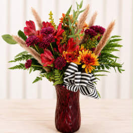 Mixed red and orange flowers in a red glass vase with a striped ribbon