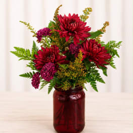 Red and purple chrysanthemum arrangement in a burgundy glass jar