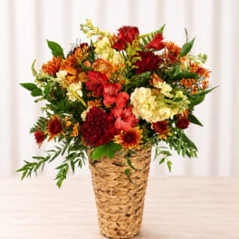 Mixed bouquet of red, orange, and cream flowers in a woven basket vase