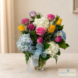 Mixed bouquet of roses and hydrangeas in a glass vase with a blue ribbon