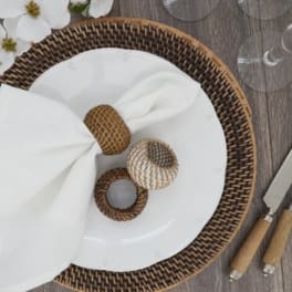 White plates with woven napkin rings on a wicker charger