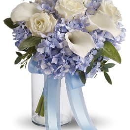 White roses and blue hydrangeas in a glass vase with a blue ribbon