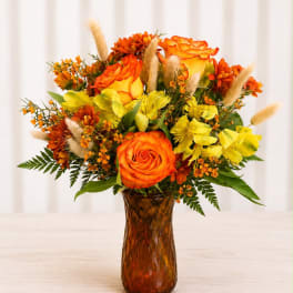 Orange and yellow flower arrangement in an amber glass vase