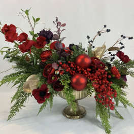 Red floral arrangement in a gold pedestal vase with berries and ornaments