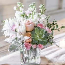 Pink and white floral arrangement in a clear glass vase with a succulent