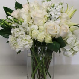 White and cream roses, hydrangeas, and lilies arranged in a clear rectangular glass vase
