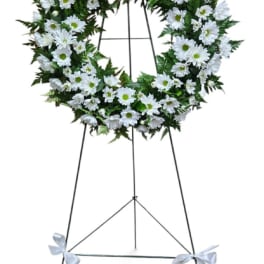 White daisy wreath on a standing easel with white ribbon bows