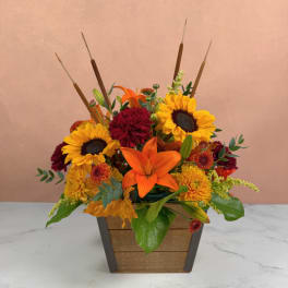 Autumn flower arrangement with sunflowers, lilies, and mums in a wooden planter