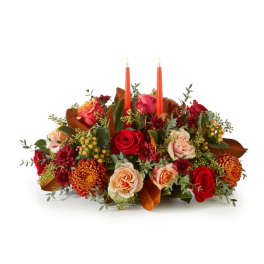 Low floral centerpiece with red and peach roses and two orange taper candles