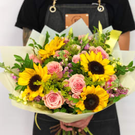 Handheld bouquet of pink roses and yellow sunflowers wrapped in pale paper