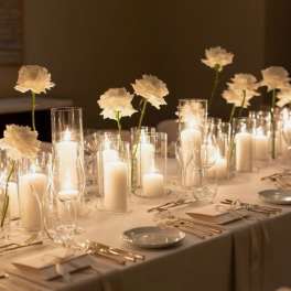 White flowers in glass cylinders with lit candles on a banquet table