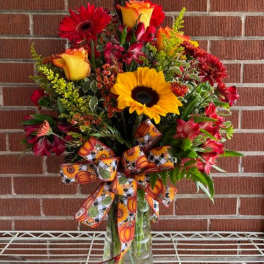 Colorful bouquet of sunflowers, roses, and gerbera daisies in a glass vase