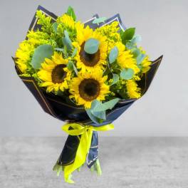 Bouquet of yellow sunflowers wrapped in dark paper with a bright ribbon