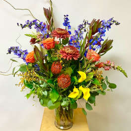Tall mixed bouquet in a clear glass vase with orange, blue, yellow, and burgundy flowers