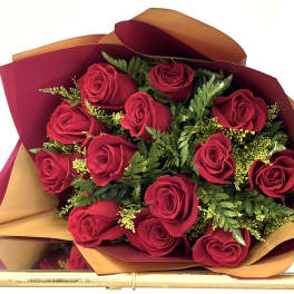 Large bouquet of red roses wrapped in pink and peach paper against a light blue background