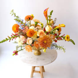 Colorful mixed flower arrangement in a gold vase on a round table