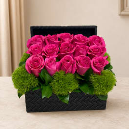 Pink roses arranged in a black woven box with green moss accents