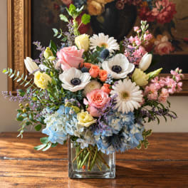 Mixed bouquet in a clear square vase with roses, daisies, and hydrangeas