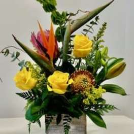 Tropical floral arrangement with yellow roses in a square vase