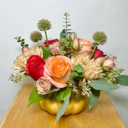 Mixed roses and chrysanthemums arranged in a gold pumpkin container