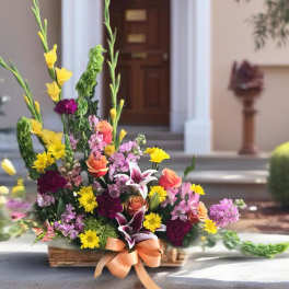 Colorful mixed flower arrangement in a basket with a peach ribbon