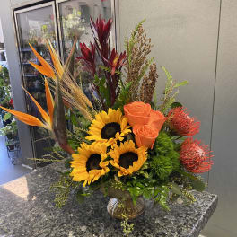 Tropical bouquet with sunflowers, orange roses, and bird of paradise in a vase