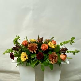 Orange and yellow mixed flower arrangement in a white container
