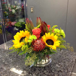 Bright mixed bouquet with sunflowers, roses, and protea in a glass vase