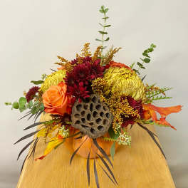 Autumn floral arrangement with orange roses, burgundy mums, and a lotus pod