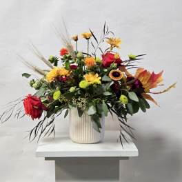 Mixed bouquet in a ribbed white vase with red, yellow, and orange blooms