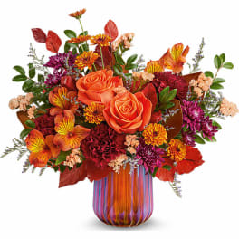 Orange roses and mixed fall flowers in a striped glass vase
