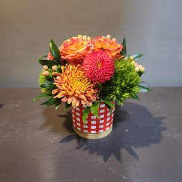 Orange and pink flowers arranged in a red-and-white container